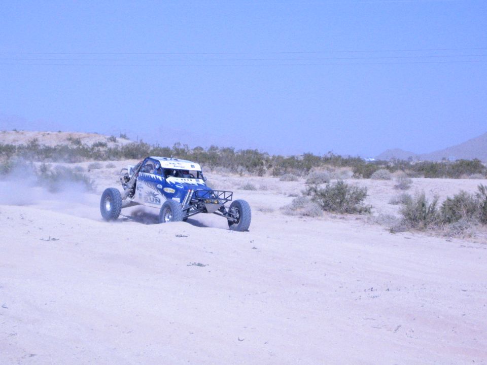 Blue and white off-road race buggy cornering on a dusty desert course