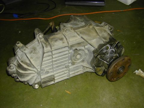 1993 Ford Bronco - A used transfer case sits on a green floor, showing signs of wear and tear.