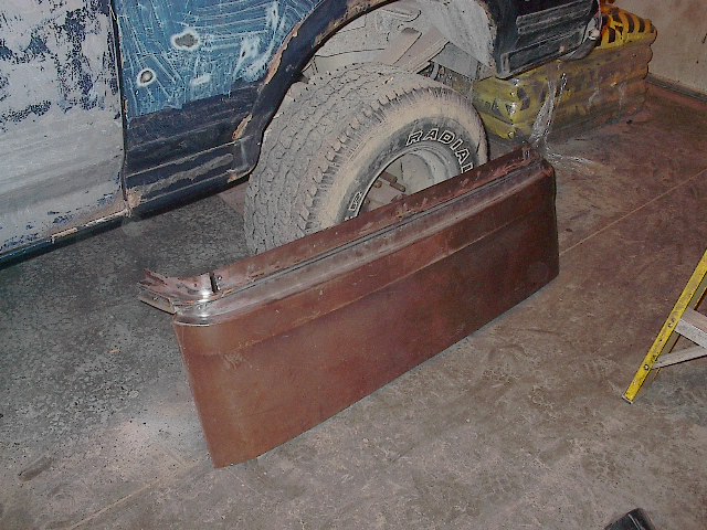 Rusty removed tailgate leaning against a primered blue truck in a garage