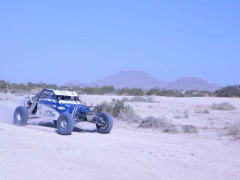Blue and white off-road buggy racing across desert with a mountain backdrop