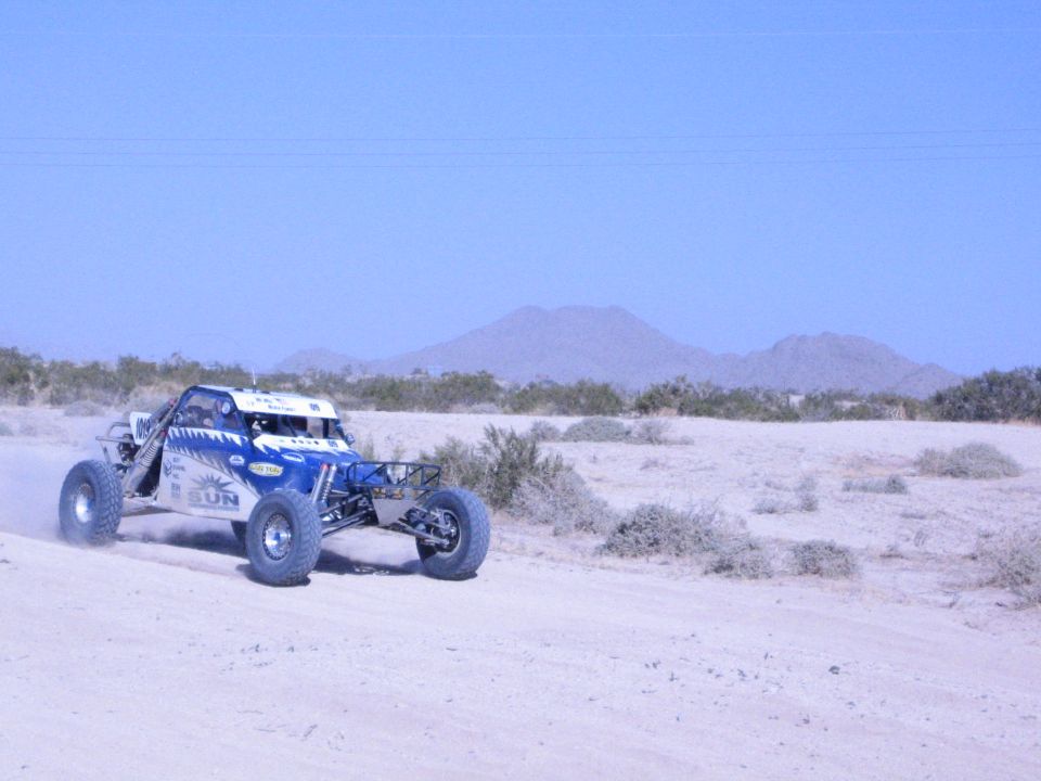 Blue and white off-road buggy racing across desert with a mountain backdrop