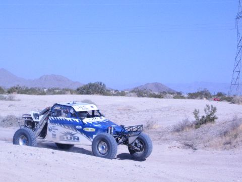 Blue and white off-road buggy number 1018 driving past power-line towers in the desert