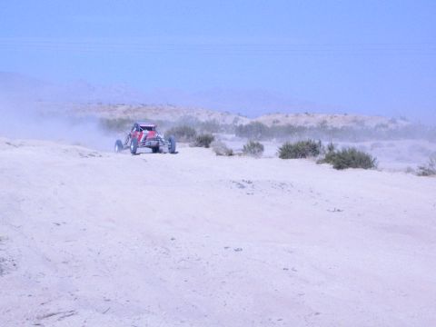 Red off-road race buggy on a distant desert trail trailing dust