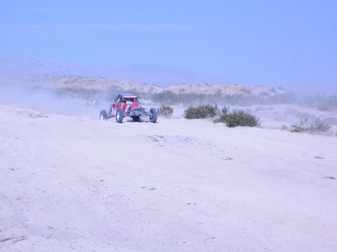 Red off-road race buggy cresting a sandy desert hill in hazy light