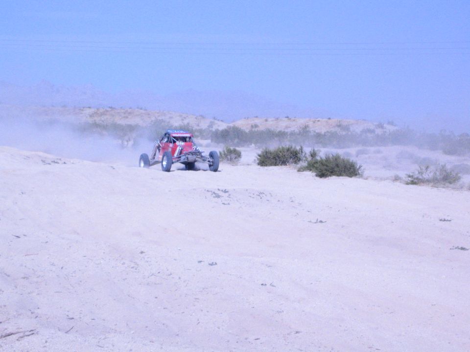 Red off-road race buggy cresting a sandy desert hill in hazy light