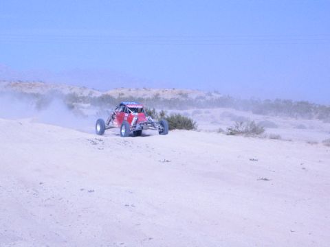 Red off-road race buggy speeding over a desert rise with a dust cloud