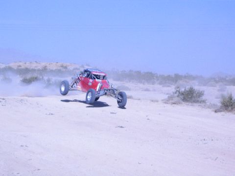 Red off-road race buggy catching air over a desert jump trailing dust