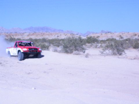 Red and white off-road race truck speeding across sandy desert trail