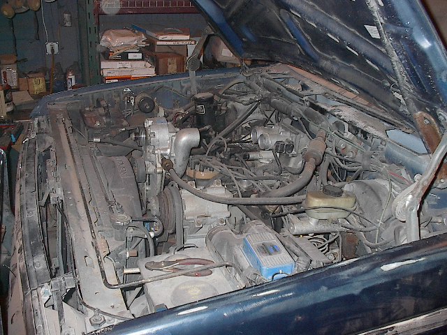 Dusty engine bay of dark blue vehicle with hood open in a garage