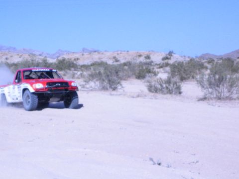 Red and white desert race truck driving on sandy track under blue sky