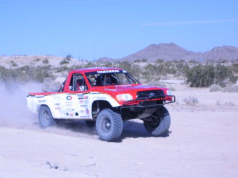 Red and white off-road race truck cornering on sandy desert course