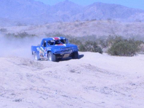 Blue off-road race truck cresting a sand berm in the desert