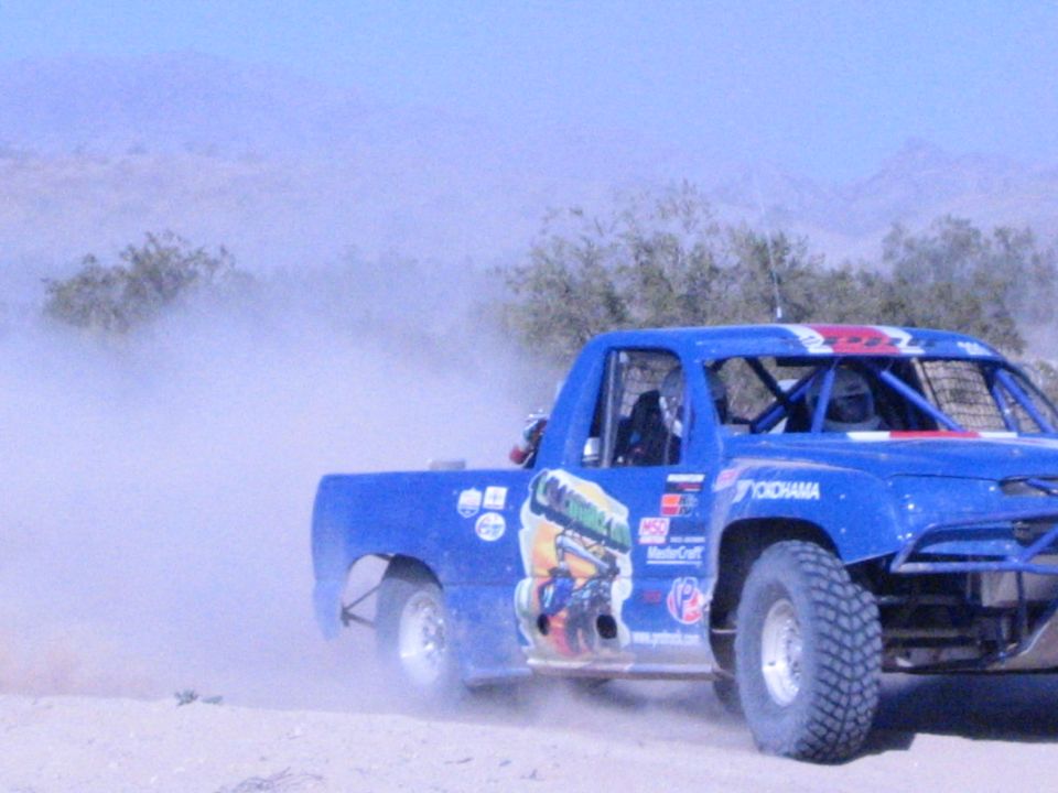 Blue off-road race truck speeding through thick desert dust