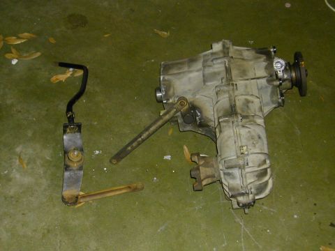 1993 Ford Bronco - A dirty transfer case and its associated linkage components are laid out on a green surface.