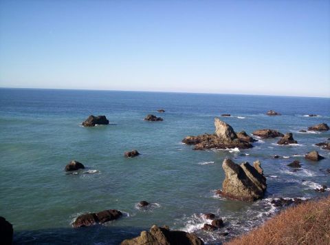 1989 Ford Bronco - A scenic view of a rocky coastline with waves crashing against the shore under a bright blue sky.