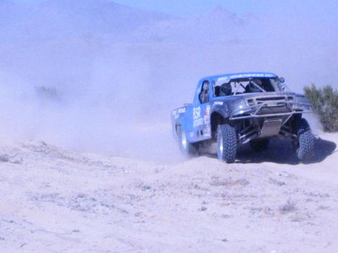 Blue off-road race truck airborne over sandy desert berm