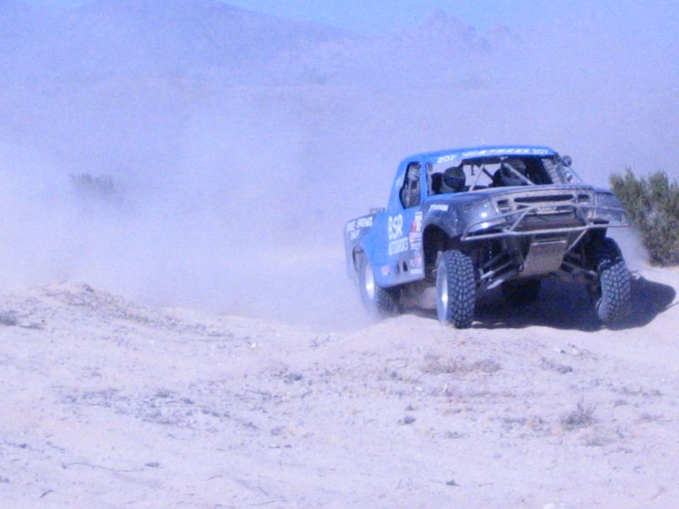 Blue off-road race truck airborne over sandy desert berm