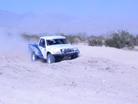 White off-road race truck driving across open sandy desert