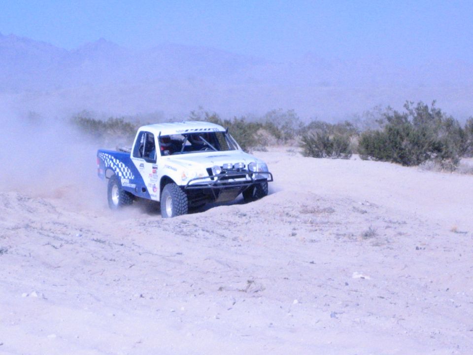 White off-road race truck driving across open sandy desert