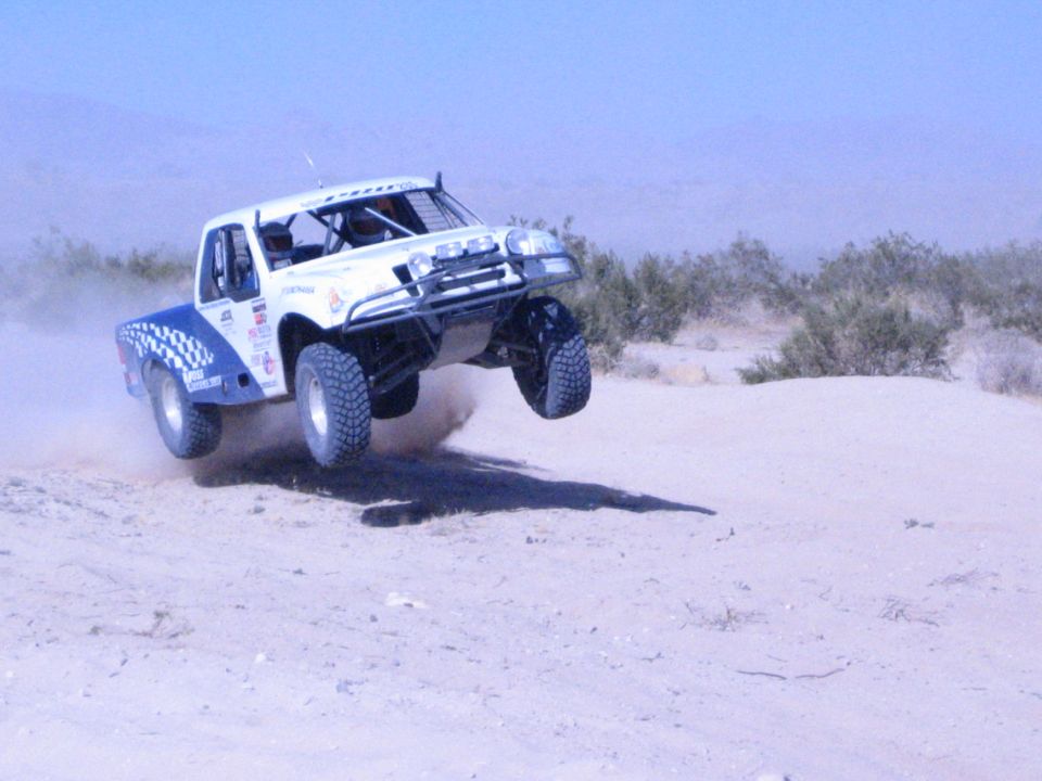 White off-road race truck airborne over a desert sand jump