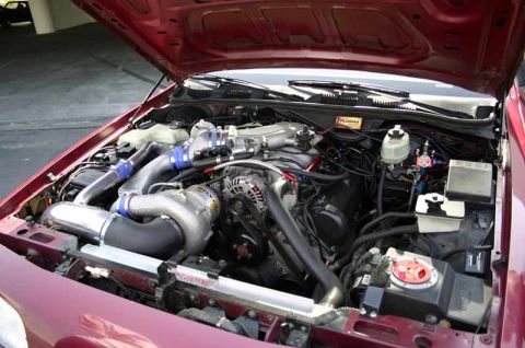 1992 Ford Crown Victoria - Open engine bay of a maroon car showing a belt-driven centrifugal supercharger mounted low on the passenger side of an aluminum-cam-cover V…