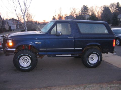 1994 Ford Bronco - Side view of a lifted blue 1994 Ford Bronco with aftermarket wheels and tires.