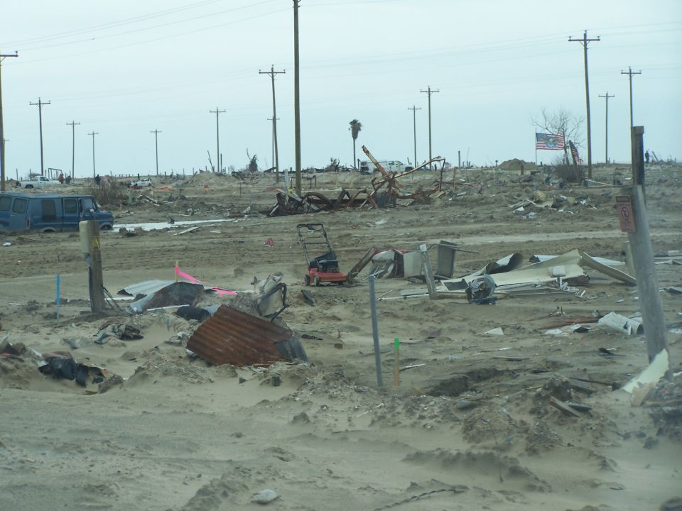 Blue van parked in a debris-filled landscape with utility poles and an American flag