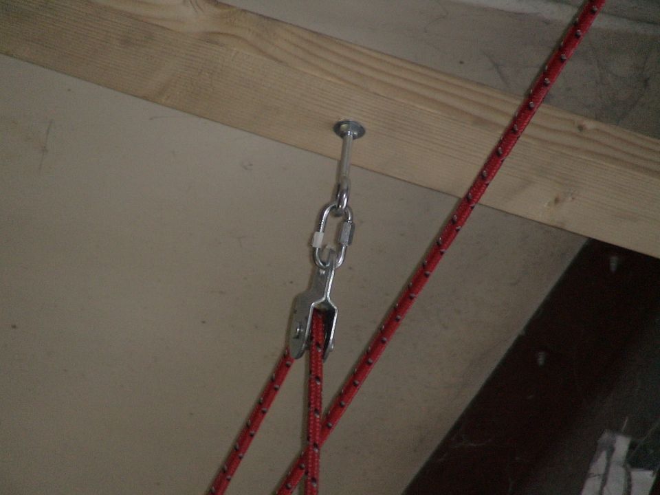Metal hook screwed into wood beam, attached to a carabiner and pulley system with red rope