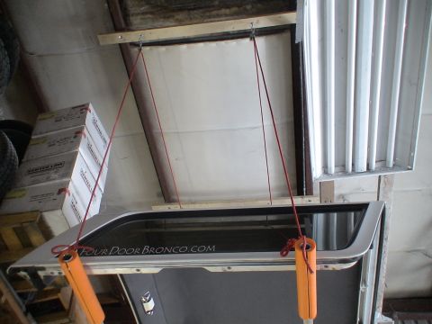1993 Ford C-350 (Centurion Conversions) - A detached rear door, possibly from a Bronco, is suspended by ropes in a garage setting.