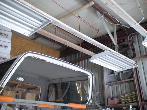 1993 Ford C-350 (Centurion Conversions) - Garage interior with fluorescent lights and the top of a vehicle's cab. Boxes labeled 'WATER LINE' are stacked.
