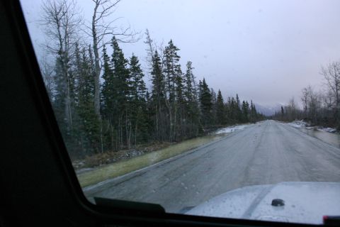 2003 Jeep TJ - Driving on a wet, grey road through a forest with snow on the sides under an overcast sky.