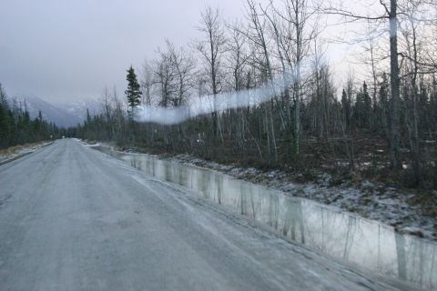 2003 Jeep TJ - A desolate, icy road winds through a forest of bare trees, with puddles reflecting the overcast sky.