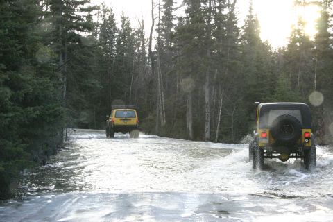 2003 Jeep TJ - Two Jeep Wranglers navigate a water-filled road surrounded by a forest.