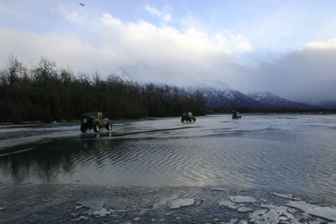 2003 Jeep TJ - Multiple Jeep TJ-style vehicles traverse a frozen landscape under a cloudy sky with snow-covered mountains in the distance.