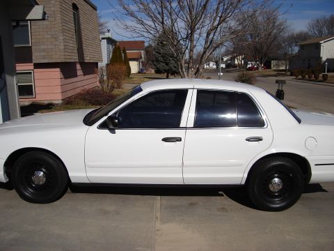 2000 Ford Crown Victoria - A white 2000 Ford Crown Victoria is parked outside a suburban house on a sunny day.