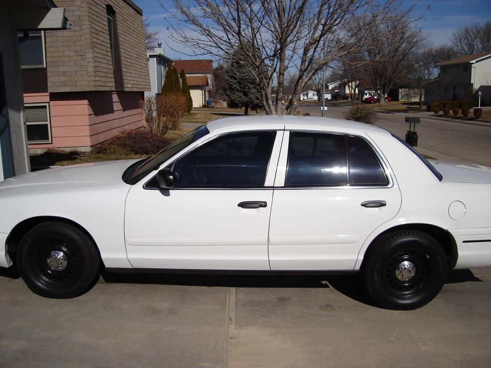 Side view of a white 2000 Ford Crown Victoria with black wheels and tinted windows parked in a driveway