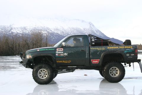 2003 Jeep TJ - A modified green pickup truck sits on a frozen surface, with a snow-capped mountain range behind it.