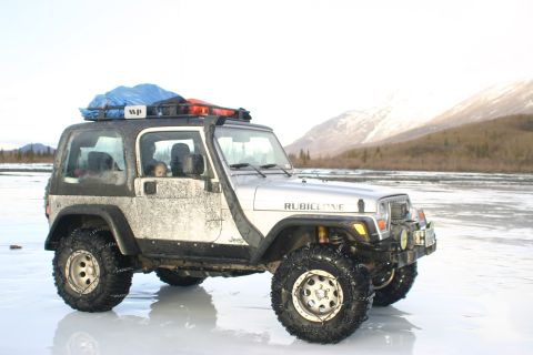2003 Jeep TJ - A silver Jeep Wrangler equipped for off-road conditions sits on a frozen surface, with mountains in the background.