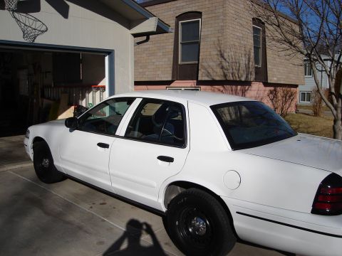 2000 Ford Crown Victoria - A white 2000 Ford Crown Victoria sedan is parked in front of a garage and house.