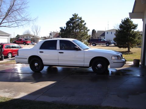 2000 Ford Crown Victoria - White 2000 Ford Crown Victoria is parked on a wet driveway with other vehicles in the background.