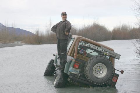 2003 Jeep TJ - Man stands on a 2003 Jeep TJ stuck in a riverbed, showing off its off-road capabilities.
