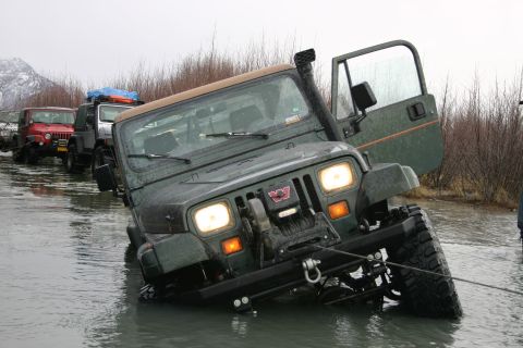 2003 Jeep TJ - Multiple Jeeps navigating through water, one appears stuck with a winch line attached.