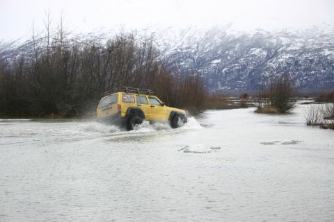 2003 Jeep TJ - A yellow Jeep Cherokee XJ navigates through a watery landscape with snow-capped mountains in the distance.