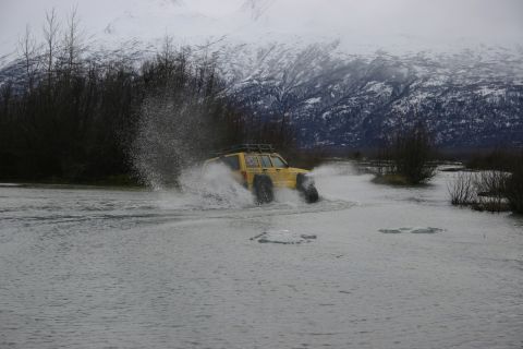 2003 Jeep TJ - A yellow 2003 Jeep TJ navigates a watery terrain, kicking up spray against a backdrop of snow-covered mountains.