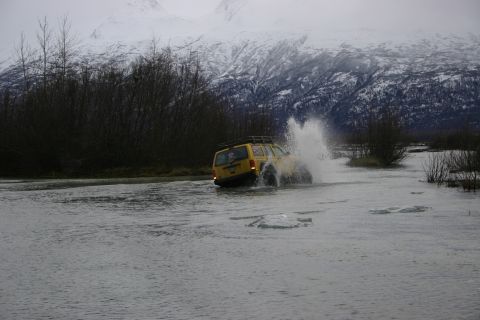2003 Jeep TJ - A yellow 2003 Jeep TJ navigates through a shallow body of water, kicking up a significant spray.