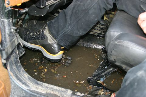 2003 Jeep TJ - The interior of a vehicle is flooded with murky water and debris, with a person's boot visible.