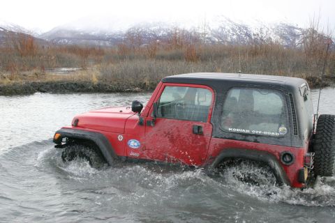 2003 Jeep TJ - A red 2003 Jeep TJ navigates through a watery landscape with snow-capped mountains in the background.