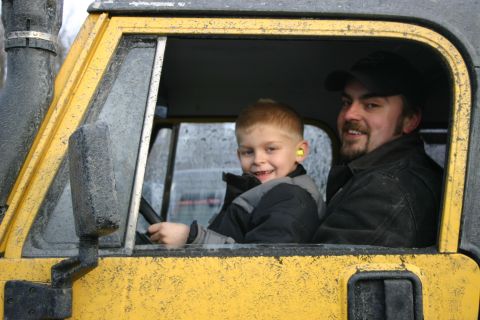 2003 Jeep TJ - A father and son sit inside a yellow vehicle, with the boy at the steering wheel and wearing ear protection.