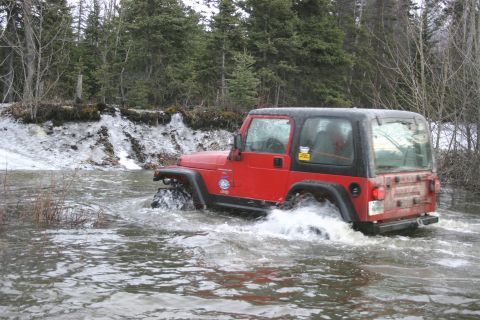 2003 Jeep TJ - Red 2003 Jeep TJ navigates through a water crossing in a wooded area.