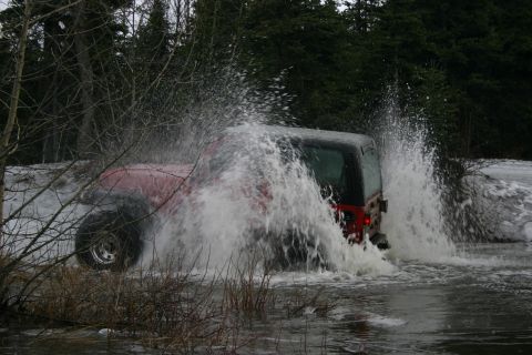 2003 Jeep TJ - A red Jeep Wrangler drives through a watery area, creating a large splash.